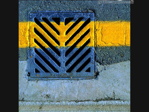 A freshly laid band of yellow road paint cutting across a metal drain grate, the image that inspired STRIPE Urban Minimal Geometric by Genevieve Staats, CreatEVE Design.