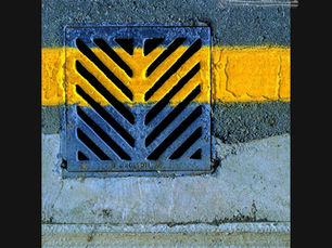 A freshly laid band of yellow road paint cutting across a metal drain grate, the image that inspired STRIPE Urban Minimal Geometric by Genevieve Staats, CreatEVE Design.