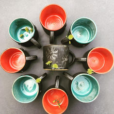 Small mugs with daisy design in relief on the outside, glazed in matt black. Insides glazed in turquoise or red.