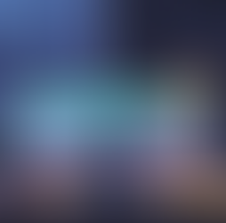 Person at desk with three monitors displaying code, in a room with a cat on a mouse pad. Rainy city view from window. Cozy ambiance.