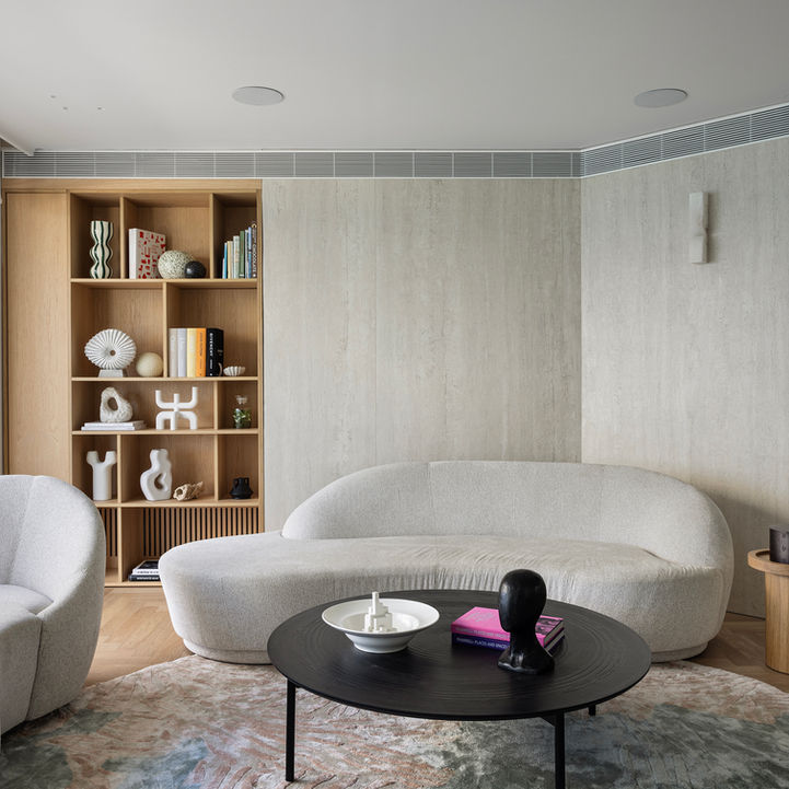Modern living room with curved sofa, bookshelves, and textured walls