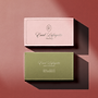 Two business cards, one pink and one green, are displayed on a textured surface. The pink card features the name "Enid Lafayette" and "Weddings," while the green card also displays "Enid Lafayette" along with contact information and "Founder & Lead Photographer."