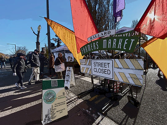 Stylized image of the Ballard Farmers Market entry. Image includes a large sign that says Farmer's Market with colorful flags on it.