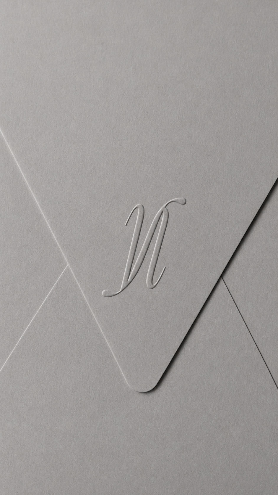 A close-up shot of a gray envelope with an embossed monogram of no filtr is shown. The envelope has a textured surface and the letter is elegant and decorative.