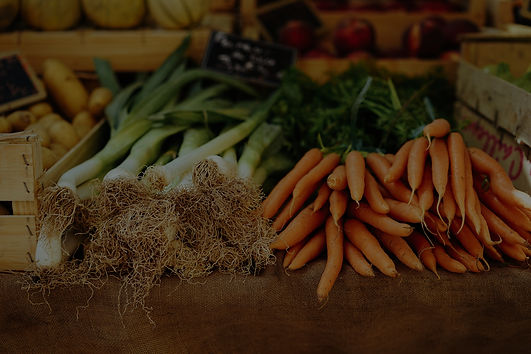 Background image of vegetables on a table at a farmer's market. Vegetables include carrots, onions, leeks.