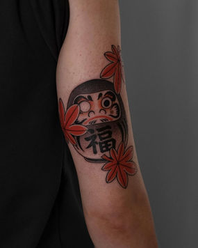 Japanese Daruma doll tattoo with shu-colored maple leaves in black and grey with red accents, custom tattoo Boston