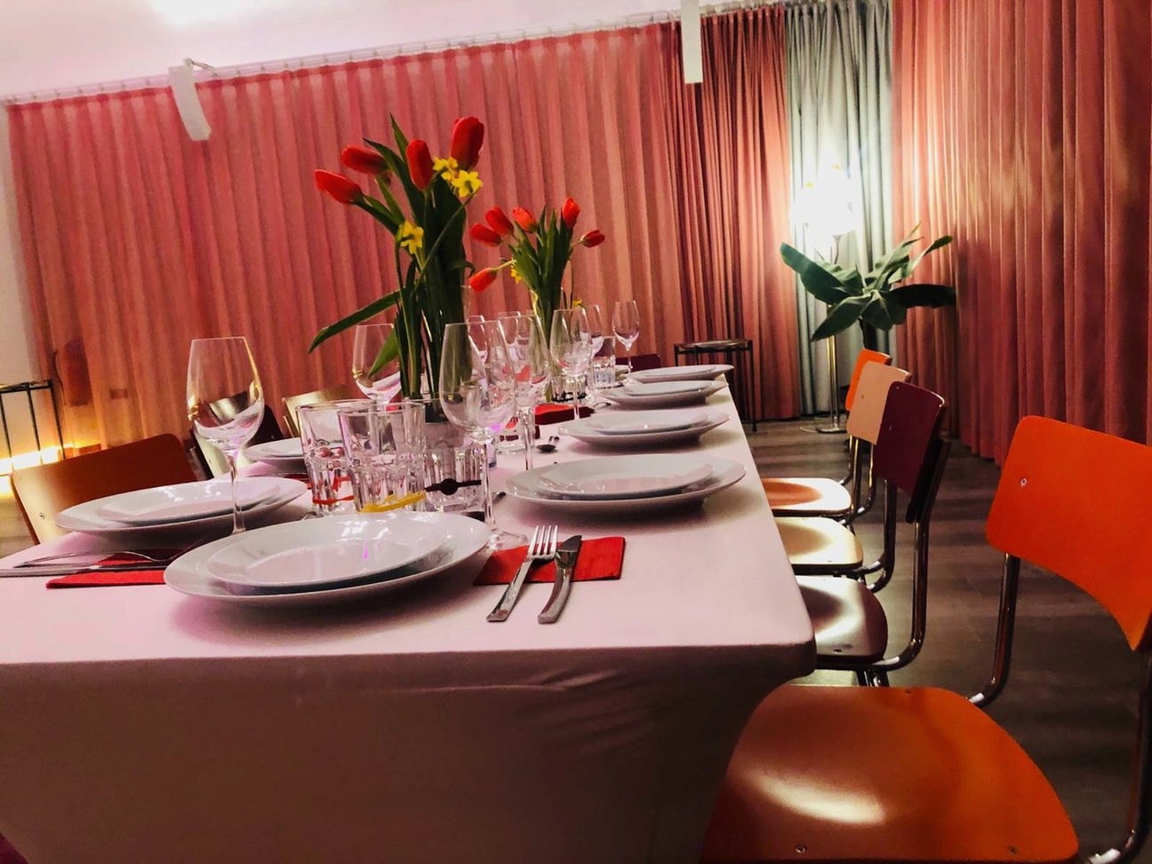 In Studio 1 ist ein wunderschön gedeckter Tisch mit Weingläsern & Blumen zu sehen. Das Licht ist sehr Stimmungsvoll angepasst und alles ist in einen Rot-Ton gehaucht.