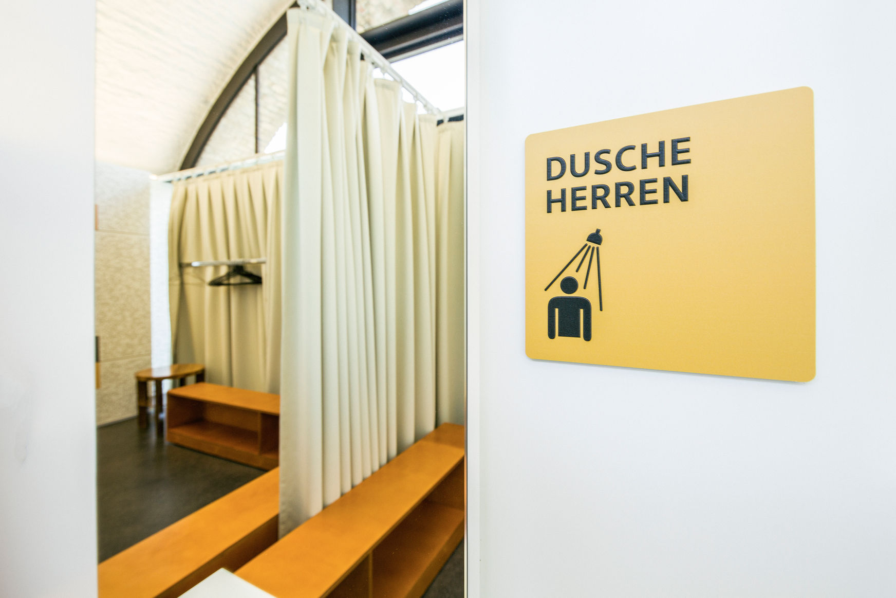 Aufnahme der Garderoben, der Vorhang zwischen den beiden Garderoben ist geöffnet, am Boden stehen in jeder Garderobe orangene Bänke.