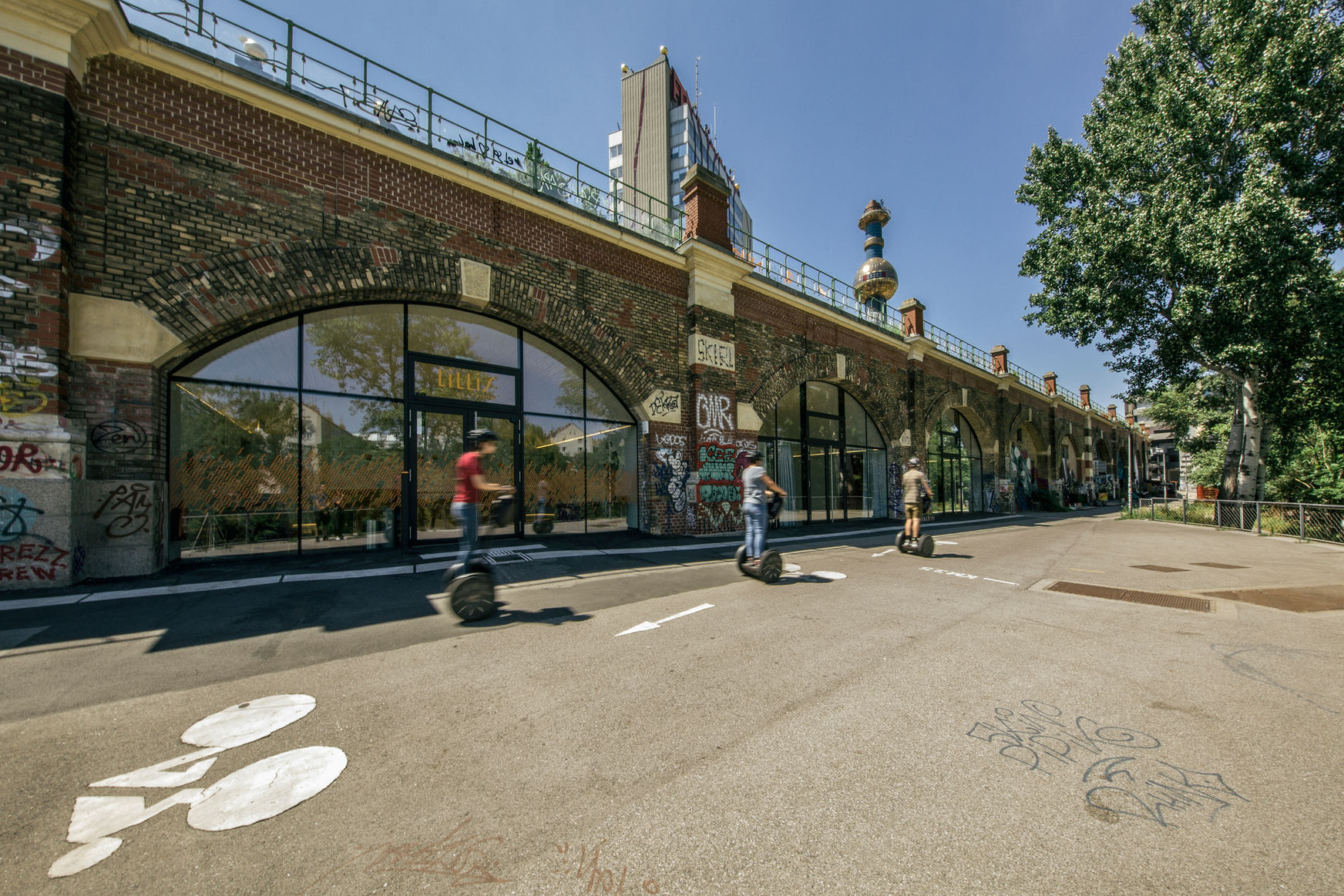 Außenansicht auf die vier Stadtbahnbögen, Segwayfahrer fahren gerader daran vorbei.