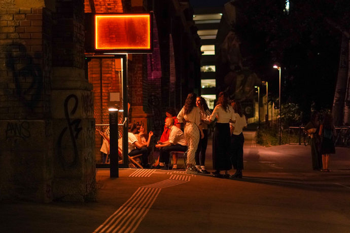 Ein Grüppchen von Leuten stehen vor der Tü im Freien und plaudert.