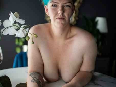 Ashley Stafford leaning over marble table topless with blue hair