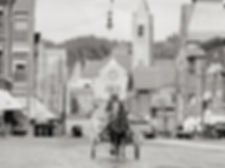 Old black and white photo of Main Street Nashua. Man guides a horese-drawn cart.