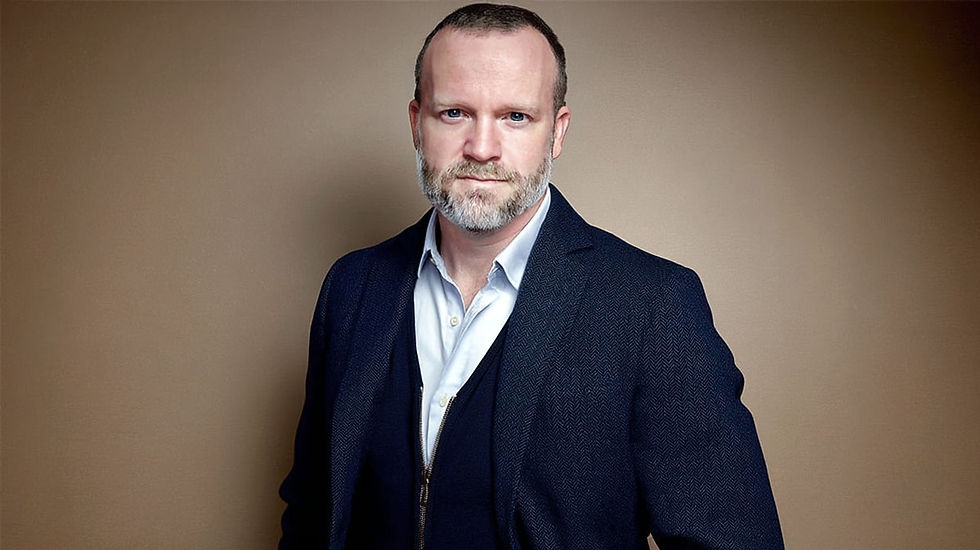 Attorney Keith F. Diaz in a white shirt, standing against a plain brown background, looking serious. Short hair and a beard. Apis Law Personal Injury Attorney