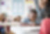 A child in a classroom working on a problem with a teacher helping.