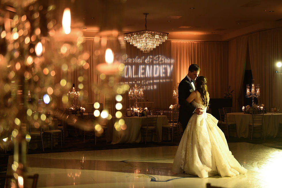 Bride and groom slow dance in a warmly lit ballroom with chandeliers, candles, and projected name text on the back curtain Bella Collina ballroom.