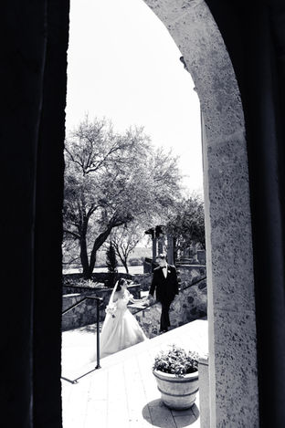 Black and white wedding photo of a bride and groom walking hand in hand through a grand stone archway at a luxury wedding venue, capturing timeless romance and elegant outdoor bridal portraits.
