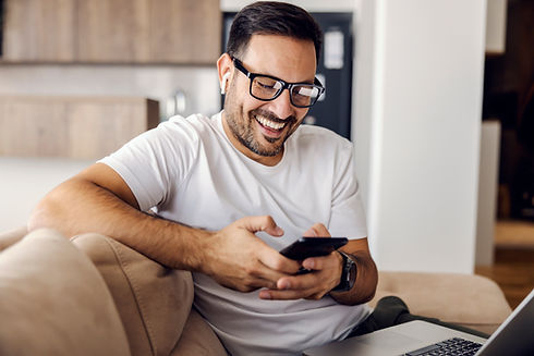 um-homem-feliz-esta-sentado-em-casa-com-o-laptop-no-colo-e-usando-o-telefone-para-enviar-m