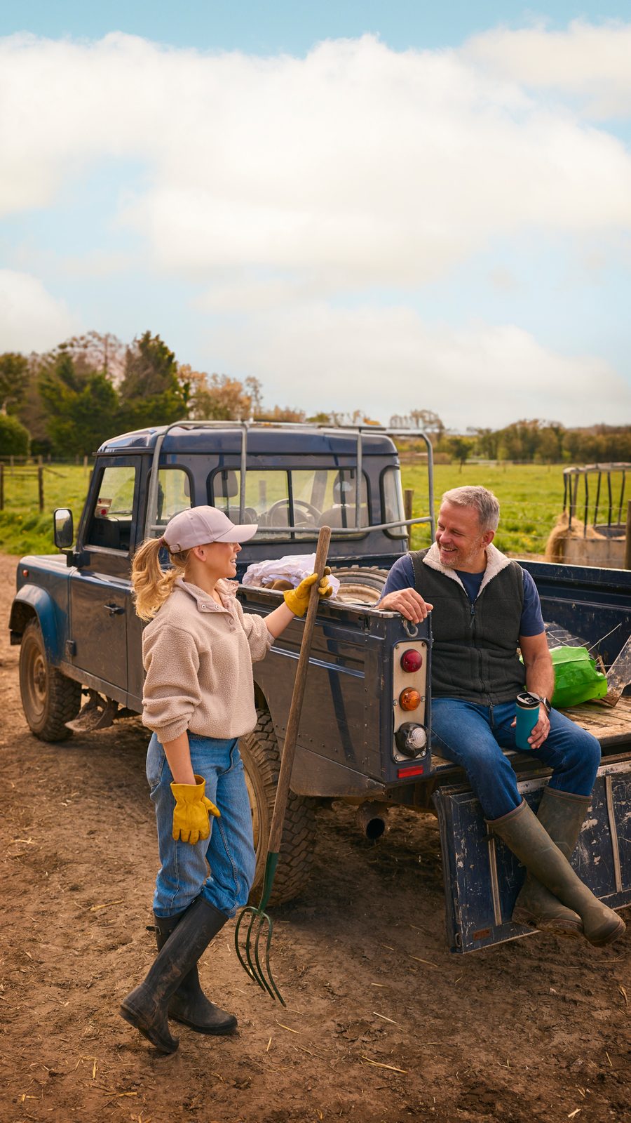 An older man sitting on a truck tailgate on a farm, talking with a woman