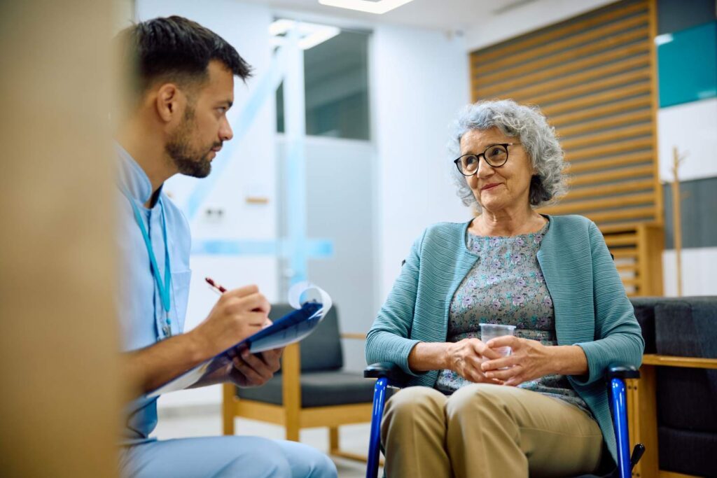 A health worker with a clipboard talking with an older woman at a clinic