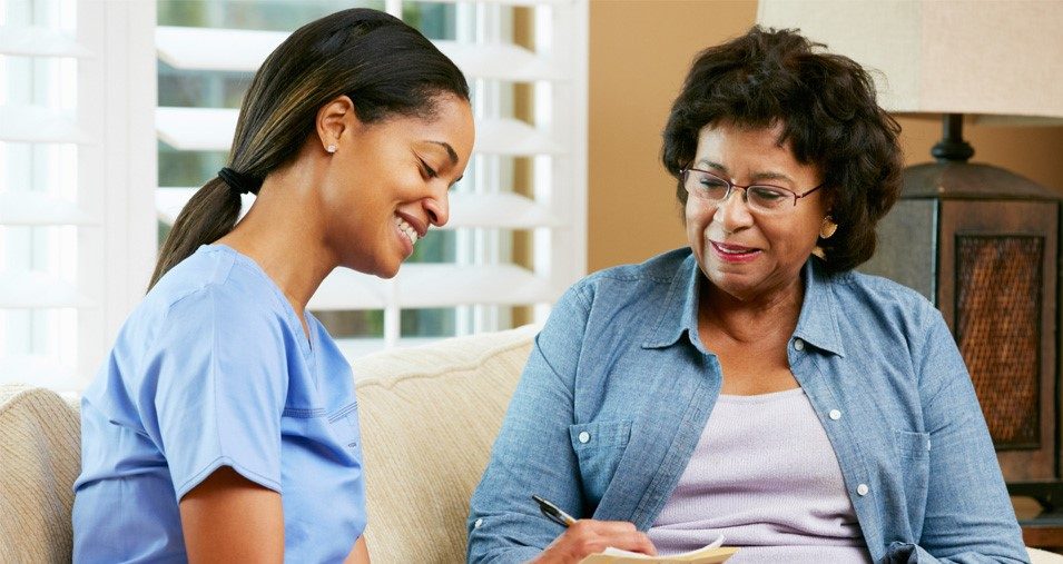 A health worker and an older Black woman smiling as they look over a form together