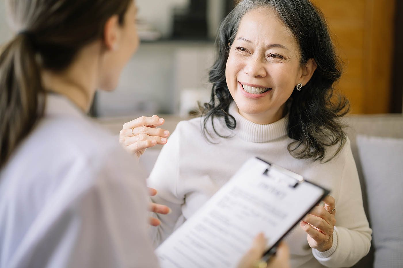 An older woman smiling and talking with a health worker who holds a clipboard