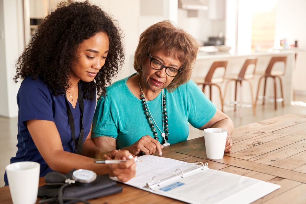A community health worker going over a binder with an older Black woman at her kitchen table