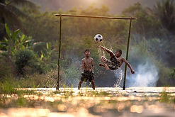 Boys playing and one shooting a goal in water filled rice paddy field