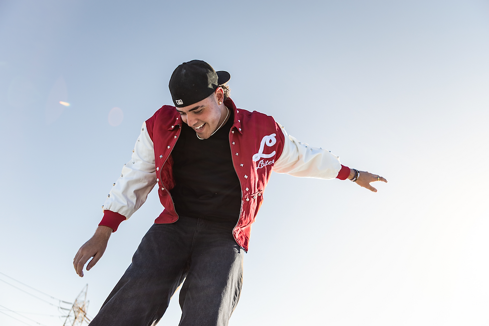 A man in a red and white jacket and a black cap joyfully balances under a clear blue sky. Sunlight highlights his cheerful expression.