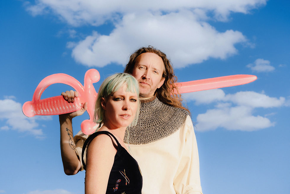 Two people pose with a pink toy sword against a blue sky with fluffy clouds, looking serious.