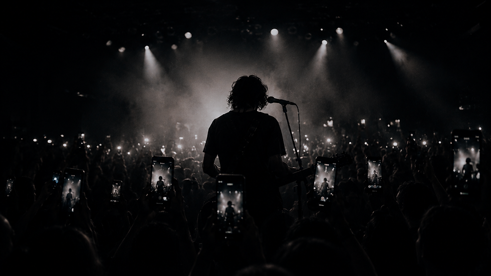 A musician performs on stage in a dimly lit venue. Audience members hold up phones capturing the moment, creating a sea of screens and lights.