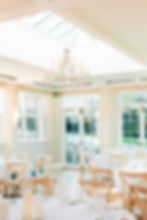 White conservatory-style wedding reception venue with dining tables and chairs and a large chandelier hanging from the ceiling at Rockbeare Manor, Exeter