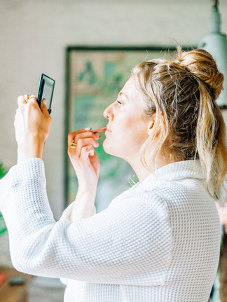 Woman with blonde bun putting on lip liner with a compact mirror in her hand.