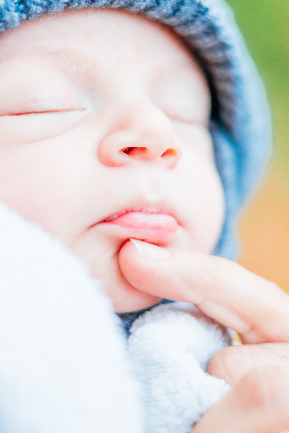 Close-up of a sleeping baby wearing a blue hat. A finger gently touches the baby's mouth, conveying a tender and peaceful mood.