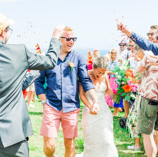 Bride and groom laughing as they walk through confetti tunnel as guests throw petal confetti into the air