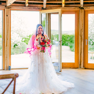 Bride stood at the top of the aisle about to walk down. She's wearing a long white gown with a hot pink veil and a pink and red bouquet at Brickhouse Vineyard, Exeter, Devon.