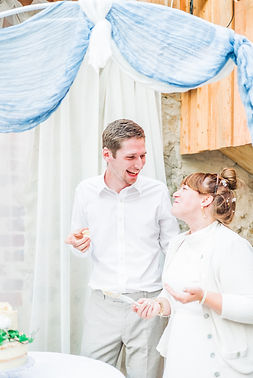 Bride and groom stood next to their wedding cake smiling at each other