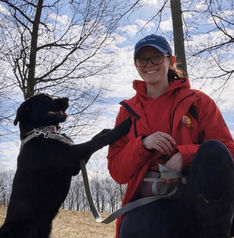 Rising Sun dog walker in a red jacket sitting outdoors with a black dog on a sunny winter walk