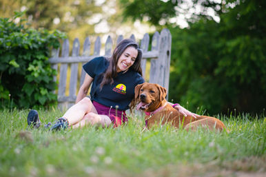 Pet sitter sitting in the grass with two dogs by a wooden fence