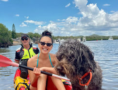 Two people in aren kayak, smiling, with a dog in the middle