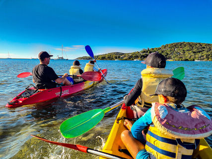 View from the back of a kayak with two kids in front and another red kayak with a man and two boys in it