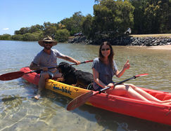 Two people in aren kayak, smiling, with a dog in the middle