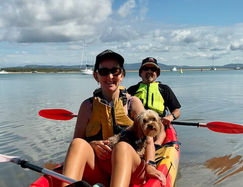 Two people in aren kayak, smiling, with a dog in the middle