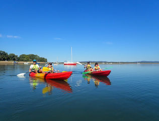 Two red double kayaks with parents and kids on very calm water in Seventeen Seventy