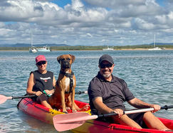 Two people in aren kayak, smiling, with a dog in the middle