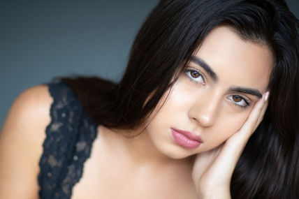 Female with dark brown hair with hand against face