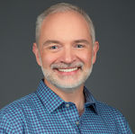 Smiling bearded man in a blue shirt, captured in a professional business portrait in San Diego.