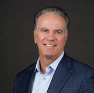 Man with navy blue pattern suit and a baby blue dress shirt with no tie and smiling