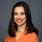 Team headshot of a woman with dark hair in an orange shirt, taken in the Carlsbad office.