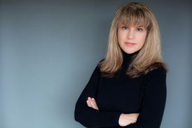 Woman with sandy brown hair wearing black blouse posing with arms crossed against a grey studio background for a San Diego professional headshot