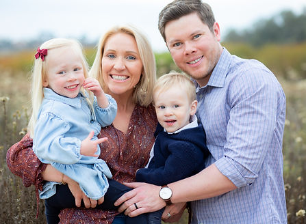 Smiling family of four poses together in an outdoor field. Family photographer.
